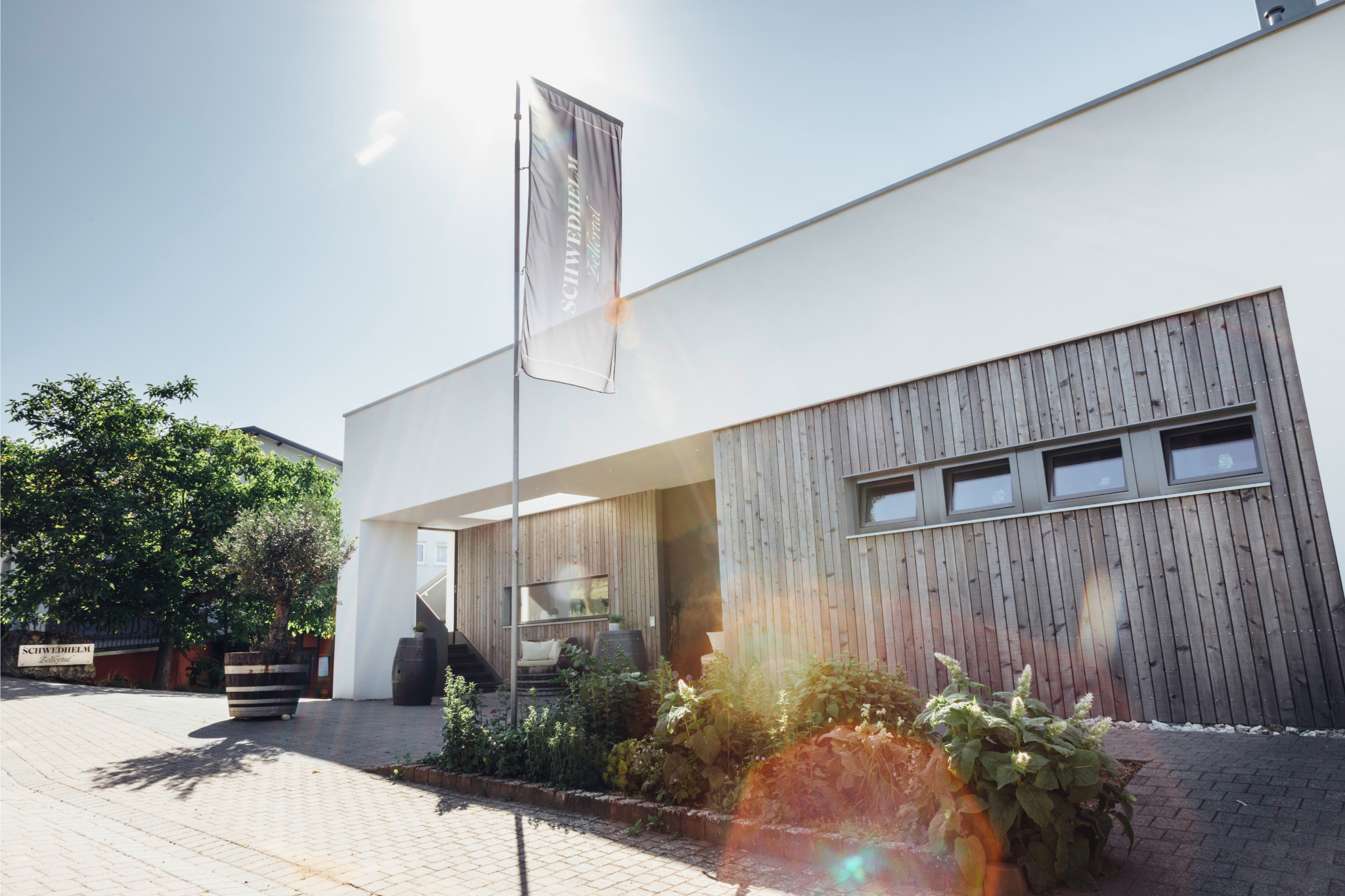 Modernes Kellereigebäude des Weinguts Schwedhelm im Zellertal mit Holzfassade, Hofeinfahrt und Flagge in der Sonne