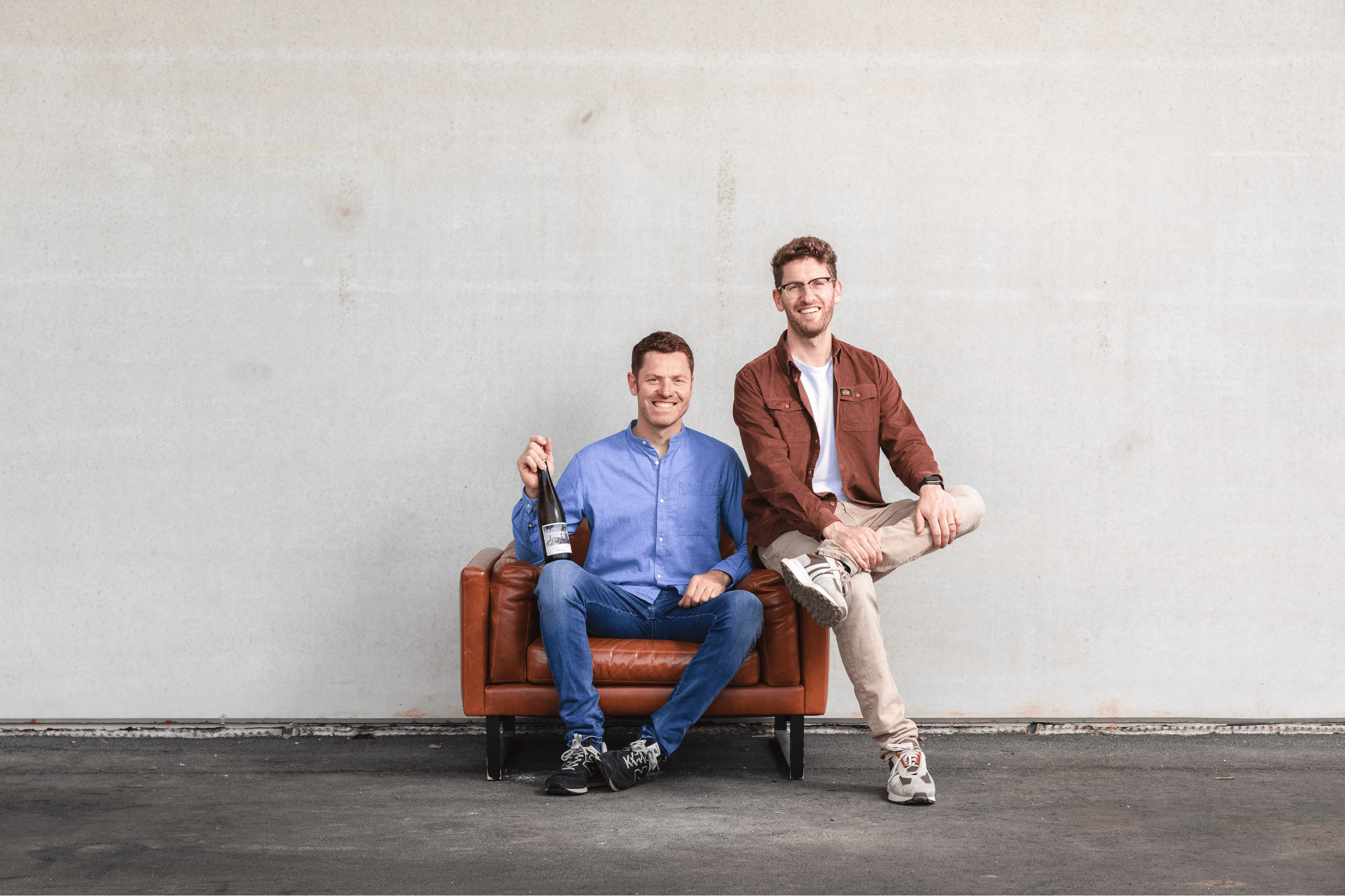 Georg und Stephan Schwedhelm, Winzer des Weinguts Schwedhelm, sitzen entspannt auf Ledersofa mit Weinflasche im Zellertal